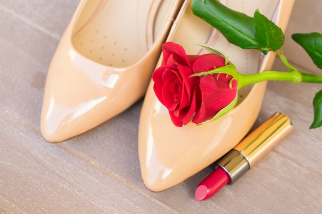 Zapatos de tacones de color nude naturaleza muerta con capullo de rosa roja y lápiz labial