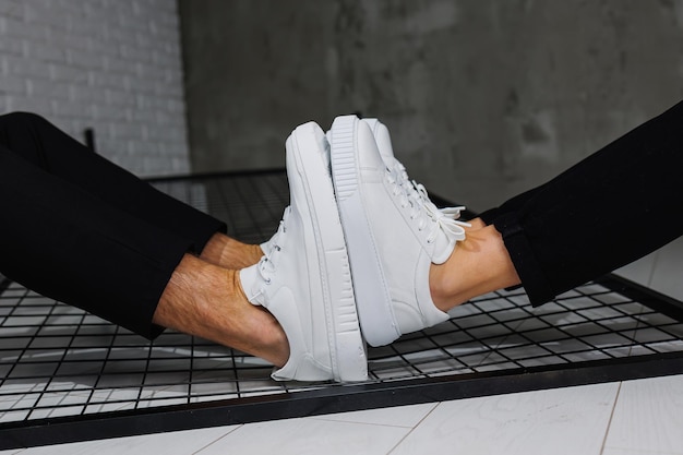 Zapatos de verano Primer plano de piernas masculinas y femeninas en pantalones negros y zapatillas de deporte casuales blancas Zapatos de cuero de verano para hombres y mujeres