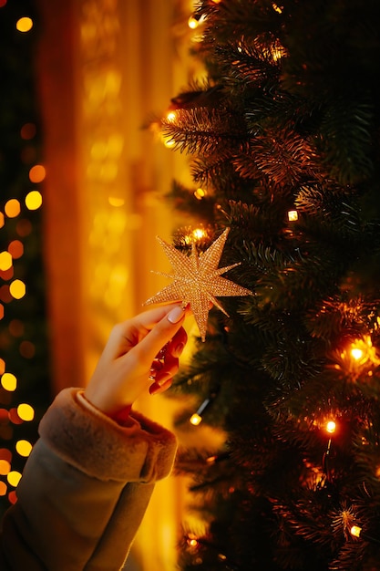 Zarte Frauenhand mit Weihnachtsbeleuchtung am Baum Festliches Weihnachtsmarkt-Winterferienkonzept