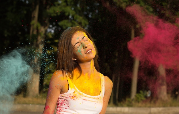Zarte junge Frau mit kurzen Haaren, die mit explodierender roter und blauer Trockenfarbe Holi spielt
