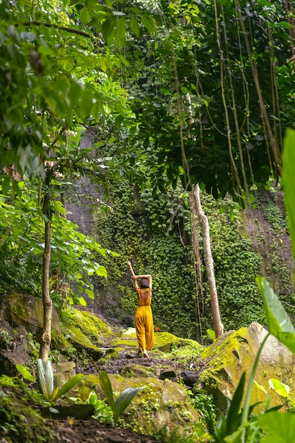 Zarte junge weibliche Person, die mit dem Rücken zur Kamera steht und den Geräuschen des Regenwaldes lauscht