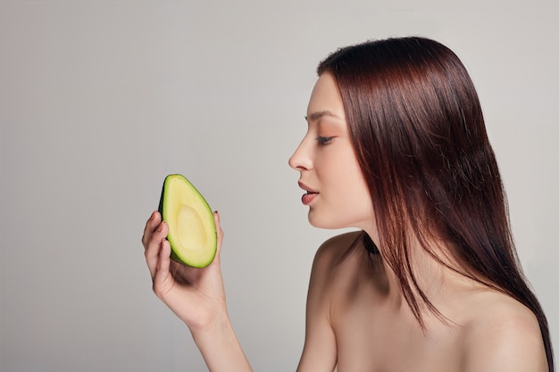 Zarte nackte Dame, die Avocado betrachtet