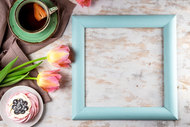 Zarte rosa Tulpen, eine Tasse Tee und Pavlova-Kuchen auf weißem Holz