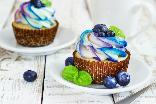 Zarte Vanille-Cupcakes mit Sahne und Beeren auf weißem Holz