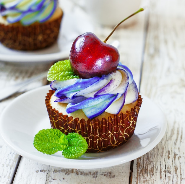 Zarte Vanille-Cupcakes mit Sahne und Beeren auf weißem Holz