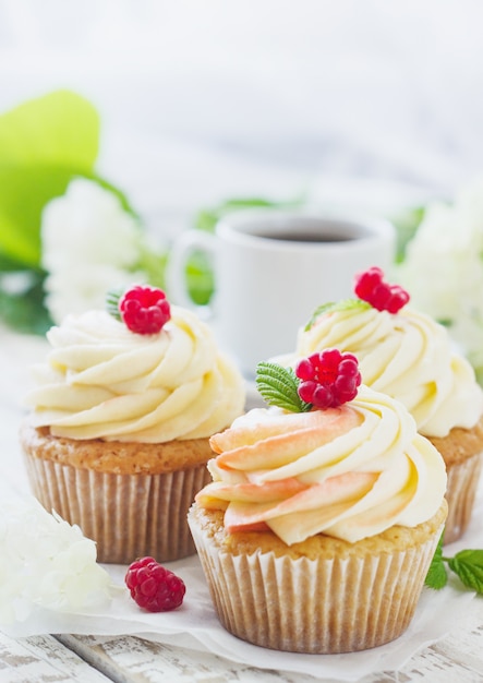 Zarte Vanille-Cupcakes mit Sahne und Himbeeren auf weißem Holz