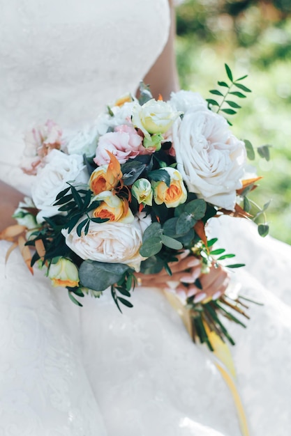 Zarter Hochzeitsstrauß in den Händen der Braut im rustikalen Stil, sonniges, klares, weißes Kleid und Rosen