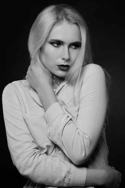 Zartes blondes Model posiert im Studio mit hellem Make-up und Folie am Hals. Monochrome Aufnahme