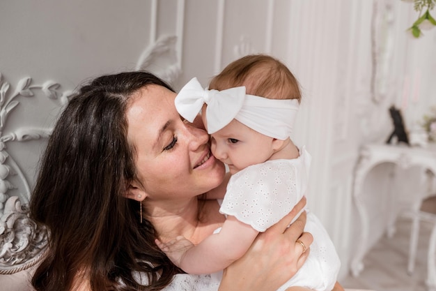 Zartes Foto einer brünetten Mutter, die ihre kleine Tochter auf dem Bett im Zimmer umarmt