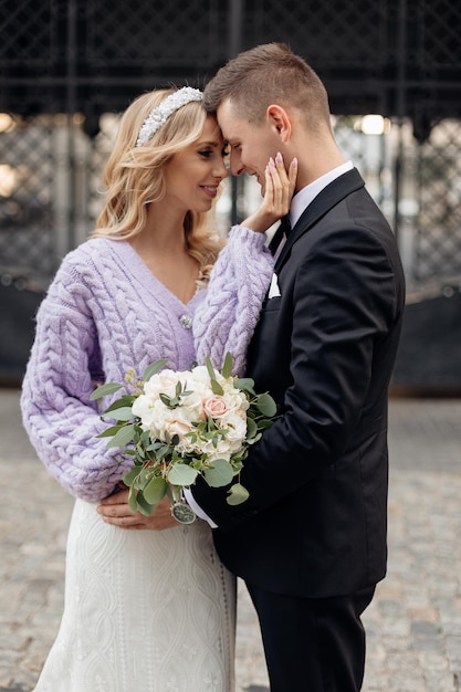 Zartes Hochzeitspaar in elegantem Anzug und Kleid spaziert durch die Stadt, hat Spaß und umarmt sich auf der Straße