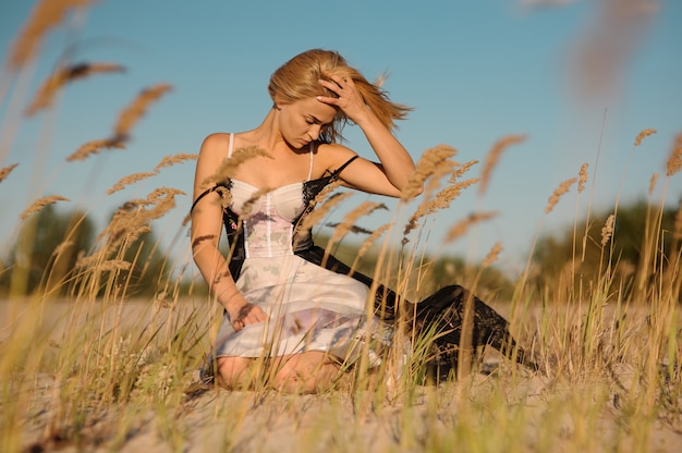 Zartes Porträt eines blonden Mädchens in einer Wäsche, die auf dem Feld sitzt