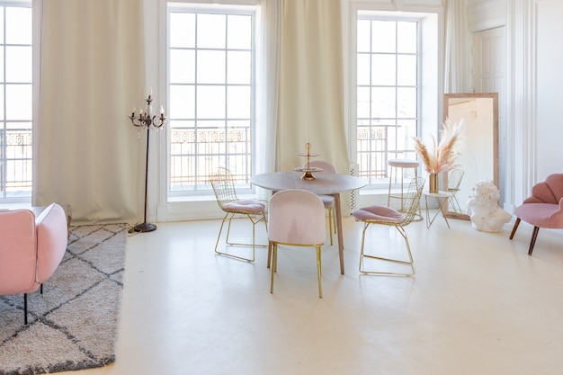 Zartes und gemütliches helles Interieur des Wohnzimmers mit modernen stilvollen Möbeln in Pastellrosa und weißen Wänden mit Stuckleisten bei Tageslicht