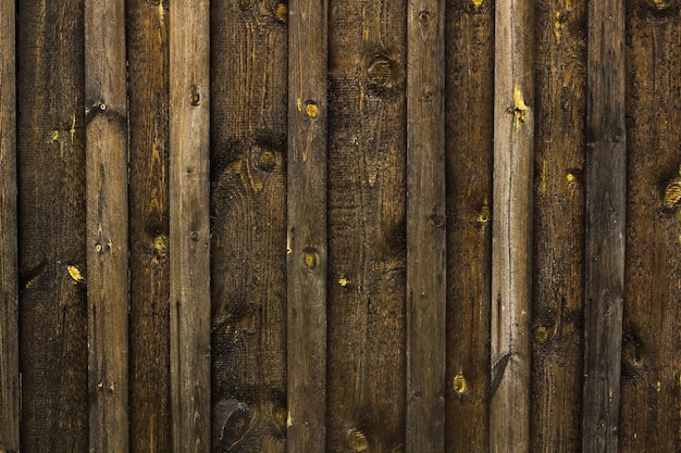 Zaun aus dunkelbraunen Holzbrettern mit Streifen und Knoten