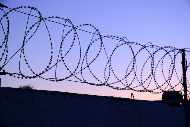 Zaun mit Stacheldrahthintergrundhimmel während des Sonnenuntergangs