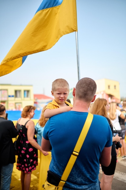 Foto zdolbuniv ucrânia 23082022 um pai segura seu filho nos braços com a bandeira da ucrânia no dia da bandeira a criança olha para a câmera há muitas pessoas por trás
