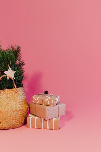 Zedernzweig im Weidenkorb auf rosa Hintergrund dekoriert. Weihnachtsgeschenke in der Nähe von Weidenkorb mit Tannenzweigen.