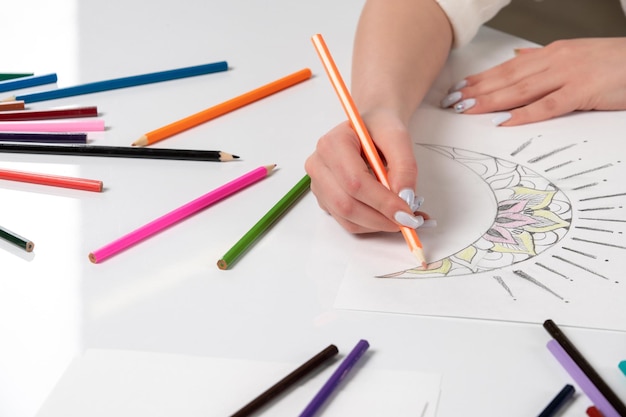 Zeichnen einer Hand eines jungen Mädchens, die einen Mond mit orangefarbenem Bleistift auf dem Tisch voller Bleistifte zeichnet