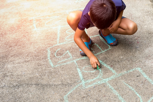 Zeichnung des kleinen Jungen mit Farbkreide auf Straßenboden