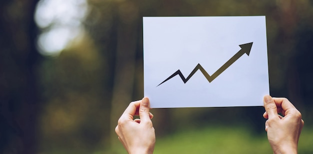 Foto zeigen sie geschäftspapierdiagrammstatistiken an, pfeil, der das diagramm in der hand auf naturhintergrund zeigt