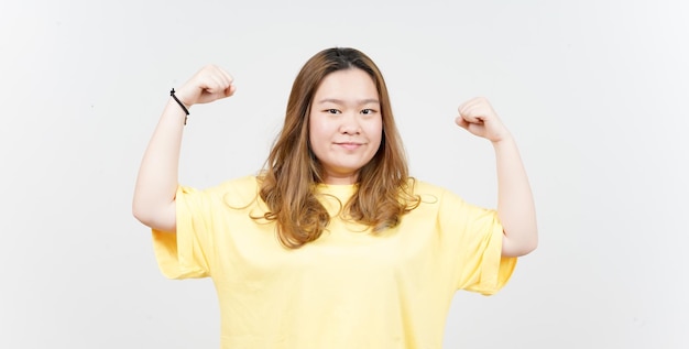 Zeigt Stärke Arme der schönen asiatischen Frau mit gelbem T-Shirt isoliert auf weißem Hintergrund