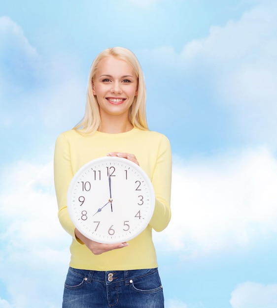 Zeit-, Bildungs- und Menschenkonzept - lächelnde junge Frau mit Wanduhr, die 8 zeigt