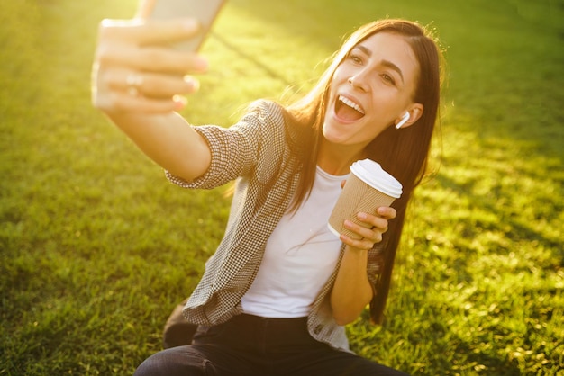 Zeit für ein Selfie Bild einer schönen, stilvollen Frau, die auf grünem Gras sitzt