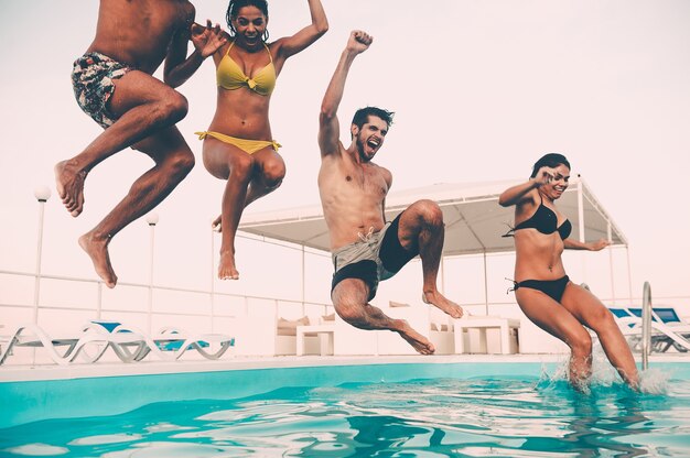 Zeit für Poolspaß. Gruppe schöner junger Leute, die glücklich aussehen, während sie zusammen ins Schwimmbad springen