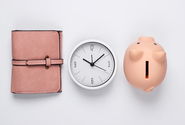 Zeit, Geld zu verdienen. Anzahlung. Weiße Uhr, Sparschwein und Geldbörse auf weißem Hintergrund. Minimalistische Studioaufnahme. Draufsicht