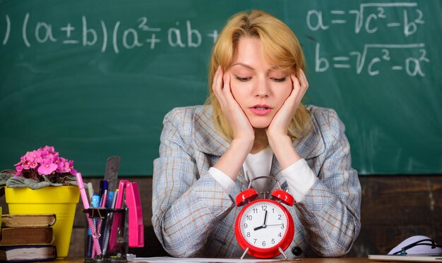 Foto zeit ist geld frau im klassenzimmer studium und bildung moderne schule wissenstag schule homeschooling müde frau zurück zur schule lehrertag lehrer mit wecker an der tafel zeit