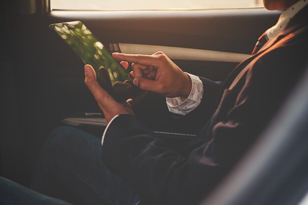 Zeit, um Entscheidungen zu treffen. Überzeugter junger Geschäftsmann, der an seinem lablet arbeitet und am Telefon beim Sitzen im Auto spricht