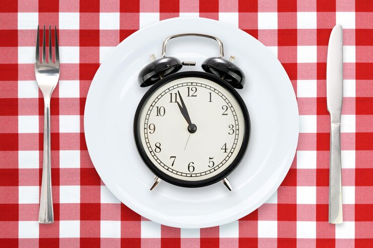 Foto zeit zum essen oder intermittierendes fastenkonzept flache lagenkomposition mit weckerplatte und utensilien auf einer rot karierten tischdecke