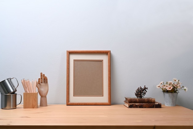 Zeitgenössischer Arbeitsplatz mit leerem Bilderrahmen, Blumentopf, Bleistifthalter und Buch auf Holztisch.
