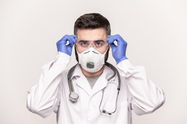 Zeitgenössischer junger Arzt in Weißmantel, Schutzhandschuhen und Atemschutzmaske, die Brillen setzen, während sie mit Patienten im Krankenhaus arbeiten