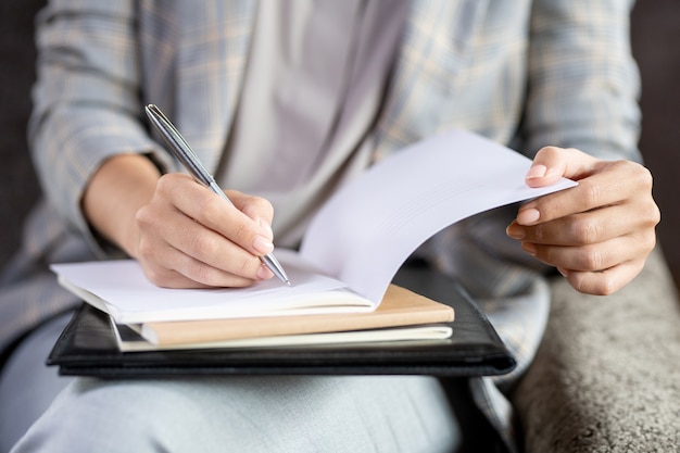 Zeitgenössischer junger Lehrer, der Stift über Seite des offenen Heftes hält, während Papier eines von Schülern prüft