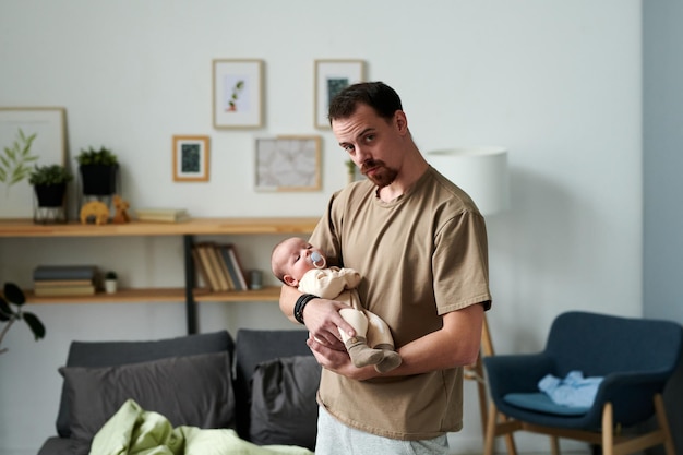 Zeitgenössischer junger Mann, der seinen kleinen Sohn einlullt, während er im Schlafzimmer steht