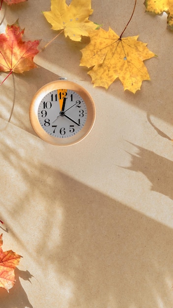 Zeitumstellung im Herbst Text Fall Back auf Tafel Kreidetafel Holzwecker mit einer Stunde Markierung mit trockenen Herbstblättern auf Recyclingkarton