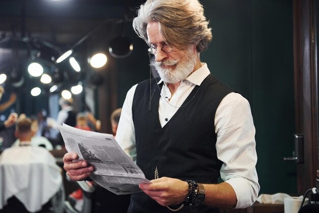 Zeitung lesen Stilvoller moderner Senior mit grauem Haar und Bart ist drinnen