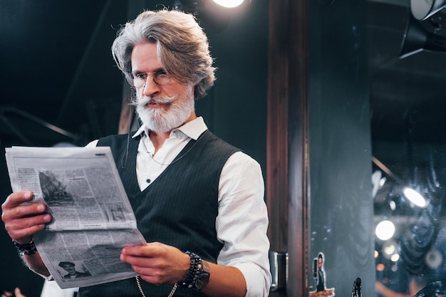 Zeitung lesen Stilvoller moderner Senior mit grauem Haar und Bart ist drinnen