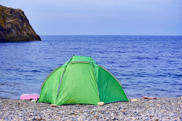 Zelt auf einem Kiesstrand vor dem Hintergrund der Felsen im Meer und Himmel.