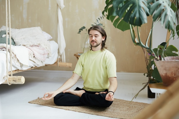 Zen-Praxis zu Hause mit Yogalehrer, gutaussehendem Meditierenden in Lotus-Pose und Yoga-Mudra, das sich zu Hause konzentriert