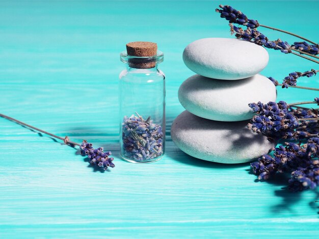 Zen-Stack-Steine auf blauem Holzhintergrund, Lavendelsamen in einer Flasche und Lavendelzweige in der Nähe.