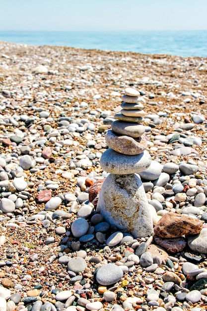 Zen-Steine, die am Strand gegen Kies, Himmel und Meer gestapelt sind