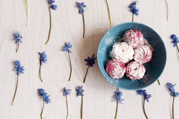 Zephyr. Kreative Food-Fotografie. Bunte Süßigkeiten im blaugrünen Teller auf Frühlingsblumen