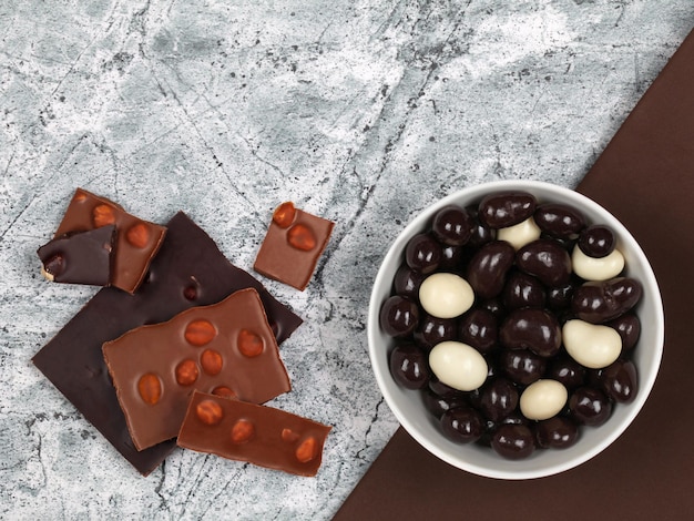 Zerbrochene Schokoriegel und mit Schokolade überzogene Nüsse auf grauem Steinhintergrund
