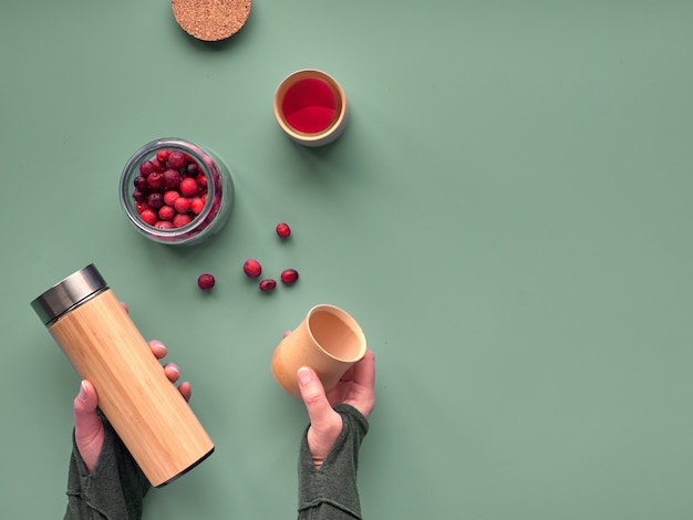 Zero desperdício de chá no balão de viagem. fazendo infusão de ervas em balão de bambu isolado eco amigável com saboroso chá de amora saudável. configuração moderna plana, mãos segurando o balão e copos de bambu, espaço de texto.