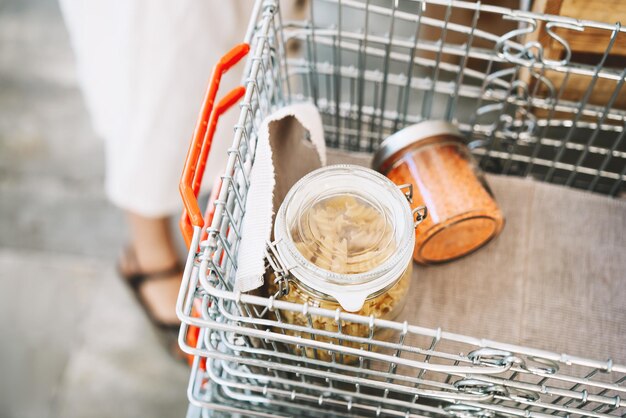 Zero desperdício de compras de alimentos cesta de metal com produtos de mercearia em frascos de vidro reutilizáveis mulher comprando produtos secos a granel em loja sustentável sem plástico conceito de baixo desperdício ecológico estilo de vida minimalista