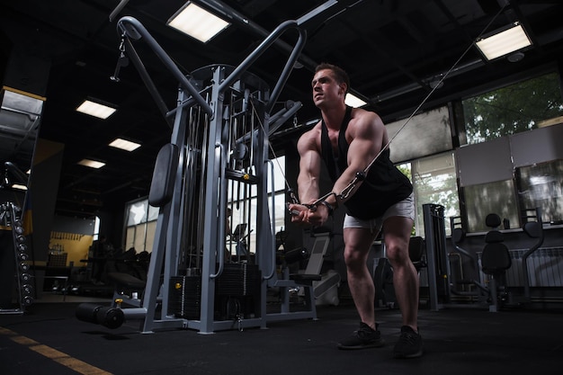 Zerrissener junger Bodybuilder, der Brustkabel-Crossover-Übungen im Kopierraum des Fitnessstudios macht