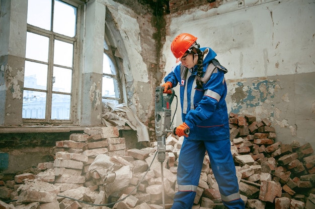 Zerstören von Geschlechterstereotypen. Tragender Helm der Frau mit verschiedenen männlichen Arbeitswerkzeugen. Geschlechtergleichheit. Mädchen, das an der flachen Umgestaltung arbeitet. Bauen, reparieren und renovieren. Frau im Männerberuf