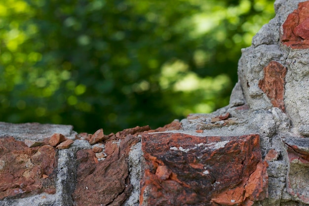 zerstörte alte Backsteinmauer mit unfokussiertem grünem Naturhintergrund