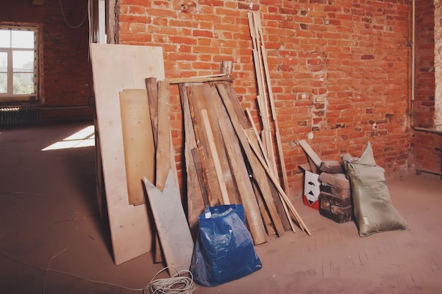 Zerstörtes Gebäude und Interieur des Industriehauses in Schutt und Trümmern an der Backsteinmauer. Holzbohlen und Taschen mit Baumüll auf staubigem Bodenhintergrund. Reparatur- und Baukonzept